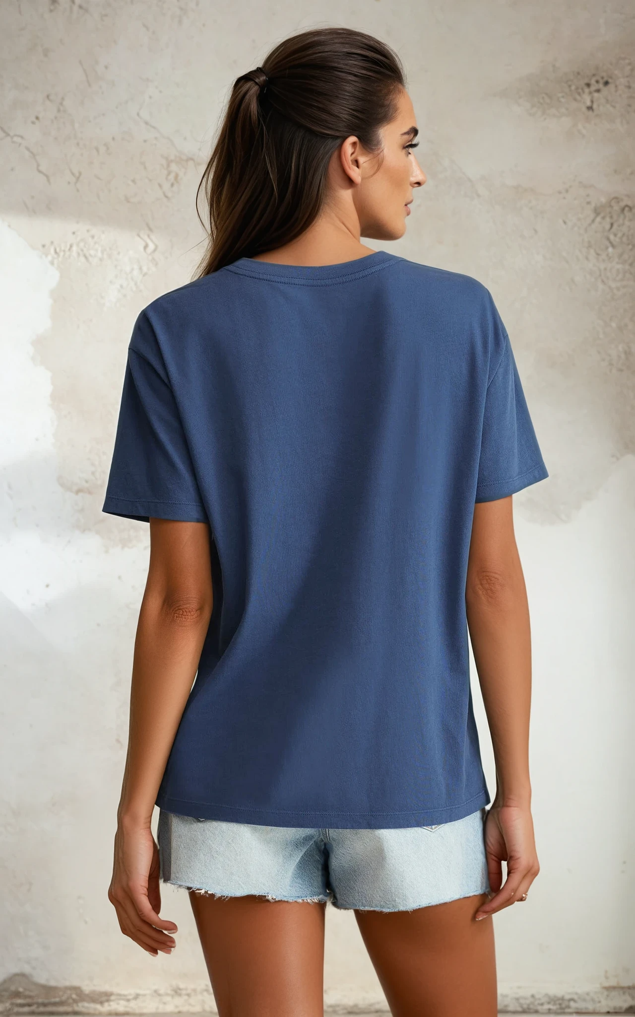Woman wearing a blue t-shirt and light denim shorts against a textured wall.