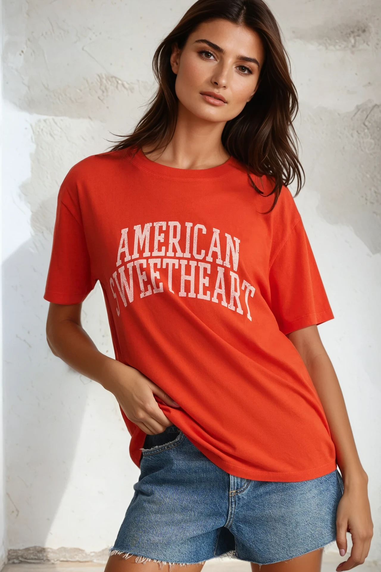 Woman wearing a red 'American Sweetheart' t-shirt and denim shorts against a light background