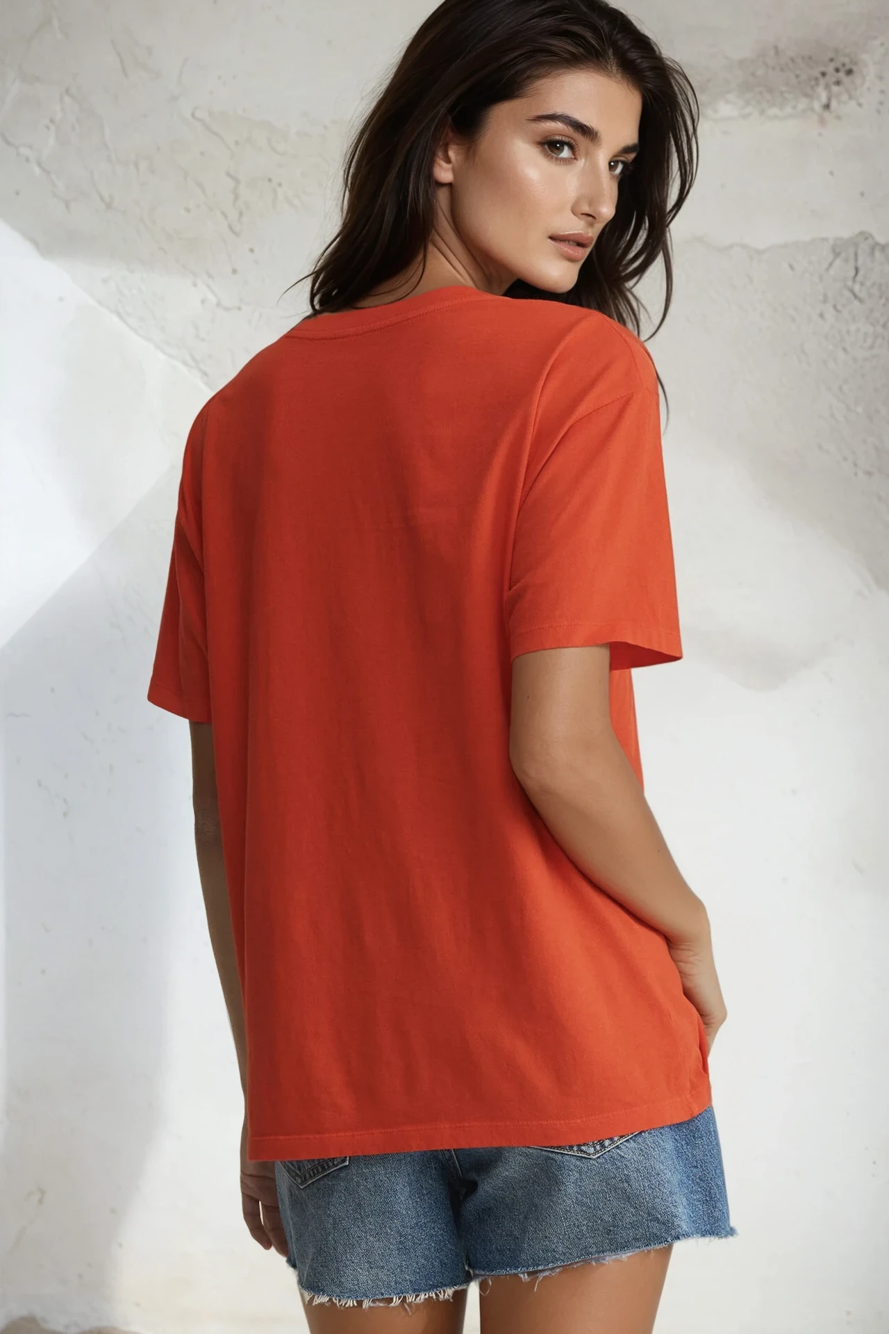 Woman wearing an orange t-shirt and denim shorts against a light background
