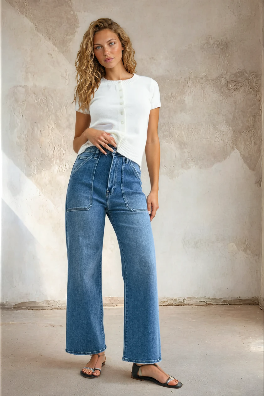 Woman wearing a white t-shirt and blue jeans against a textured wall.