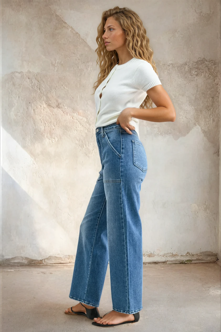 Woman wearing a white t-shirt and blue jeans against a textured wall.