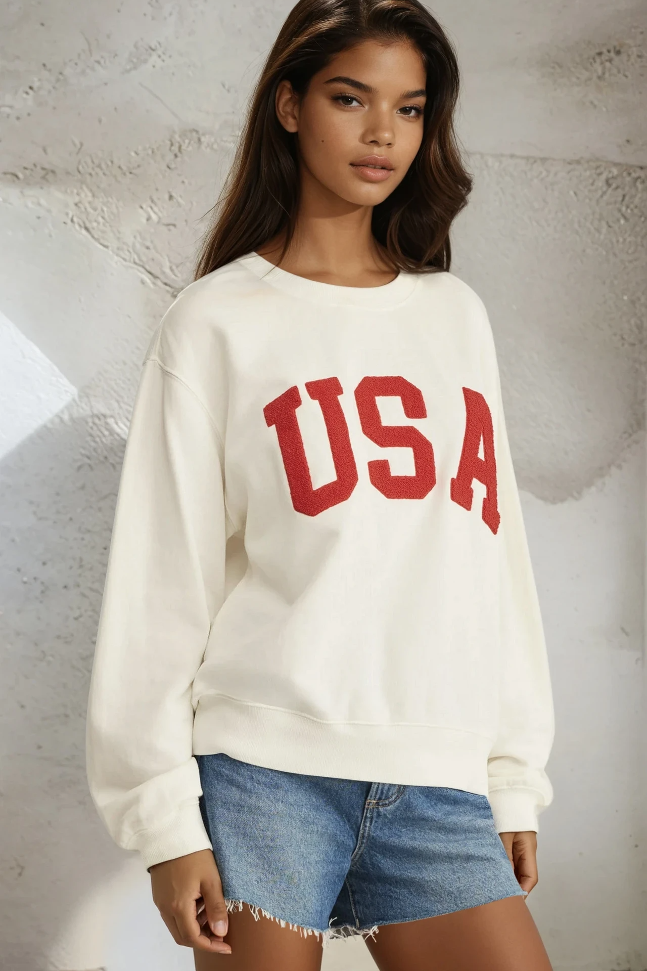 Person wearing a white sweatshirt with 'USA' in red text and denim shorts against a textured wall.