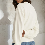 Woman wearing a white sweatshirt and denim shorts against a textured wall.