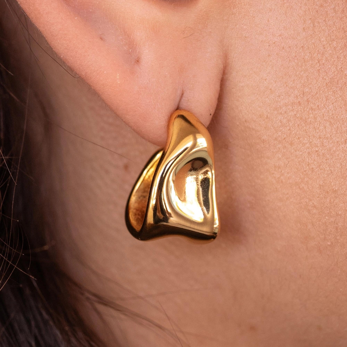 A close-up image of a person wearing a gold-colored hoop earring.