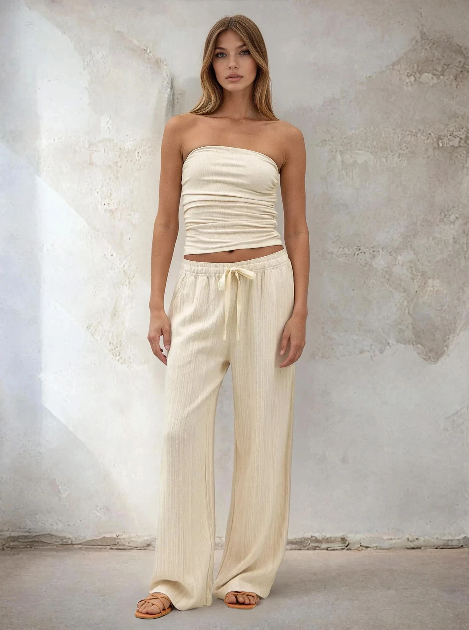 Woman wearing a strapless top and wide-leg pants against a textured wall.