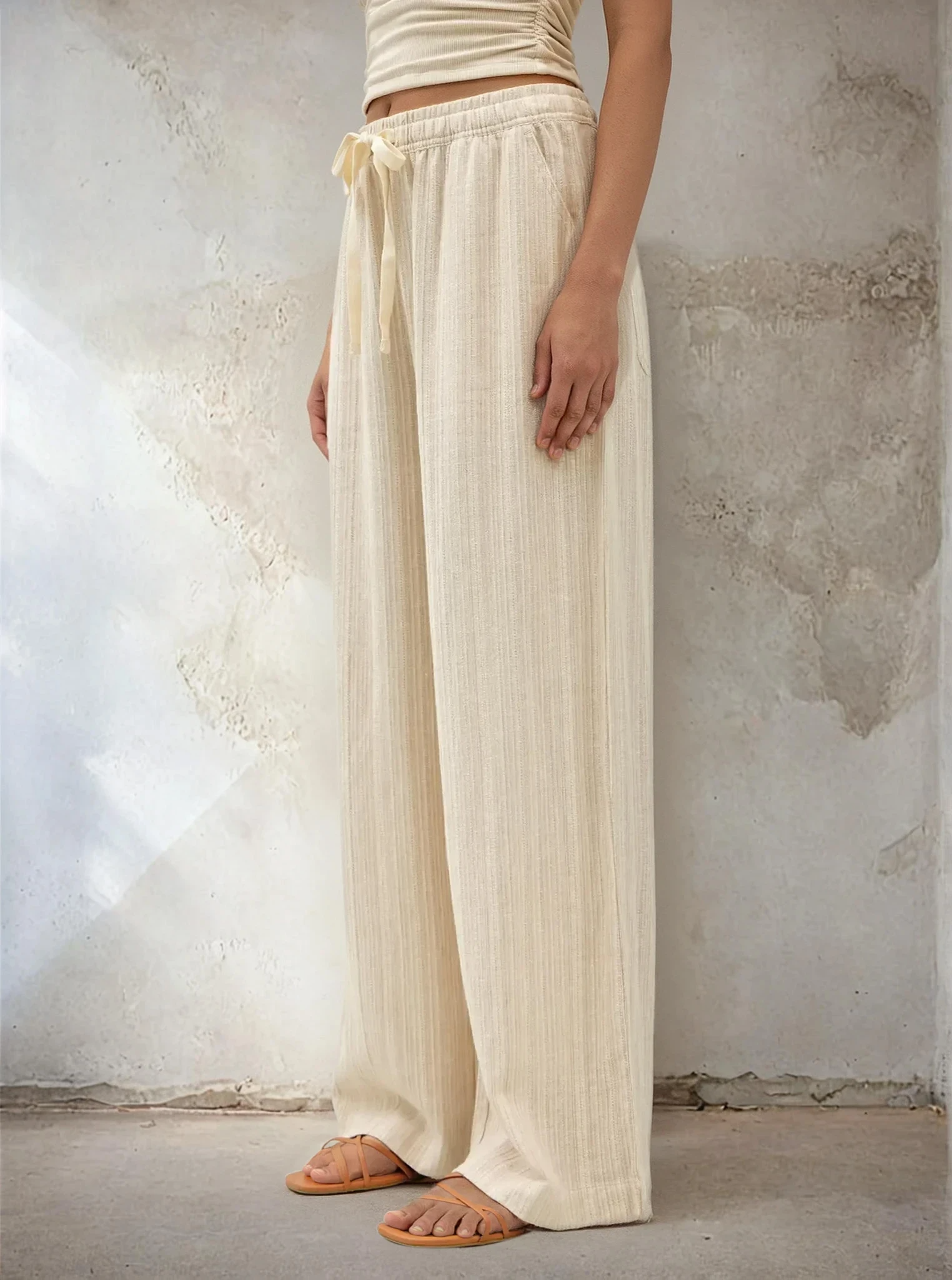 Person wearing cream-colored wide-leg pants against a textured wall.