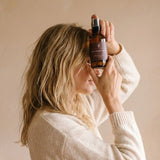 Person wearing a white sweater holding a bottle against a beige background