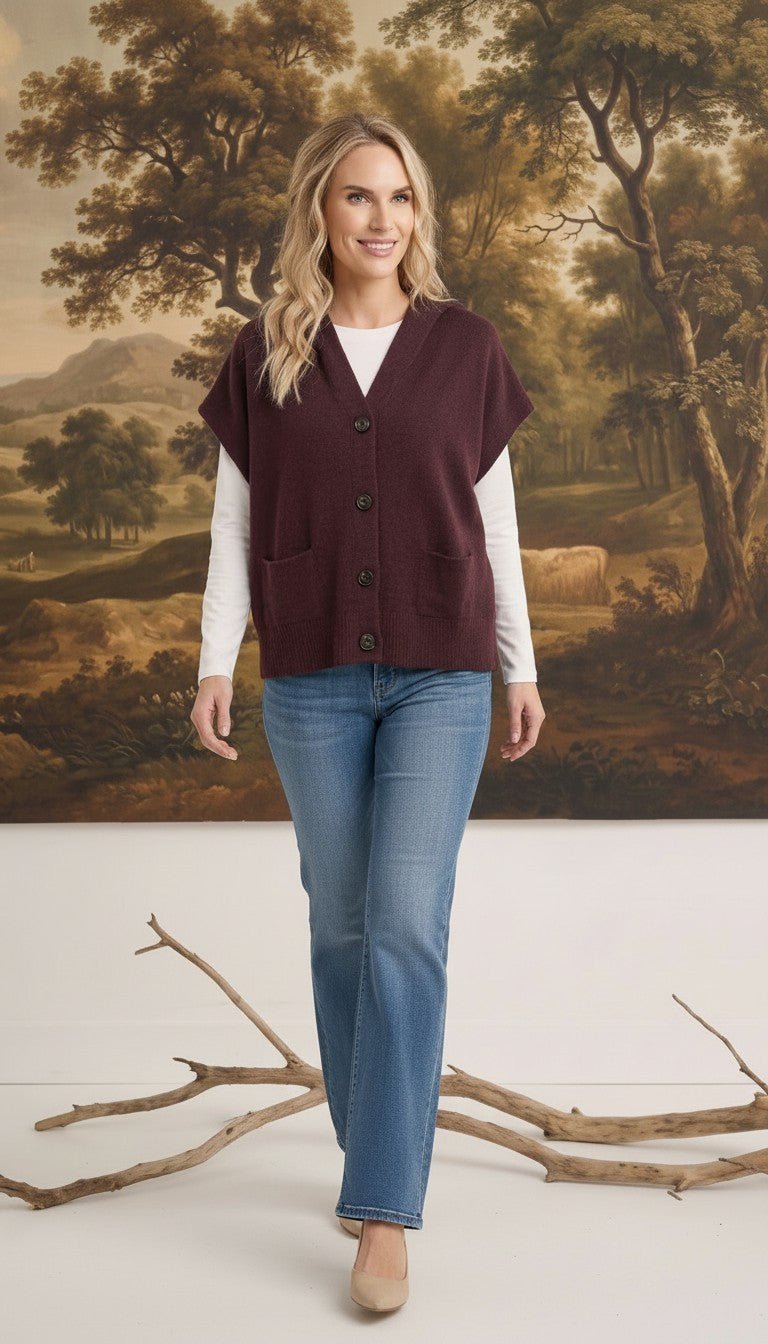 Woman wearing a graced burgundy button-down hooded vest over a white long-sleeve top and blue jeans
