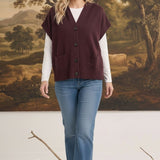 Woman wearing a graced burgundy button-down hooded vest over a white long-sleeve top and blue jeans