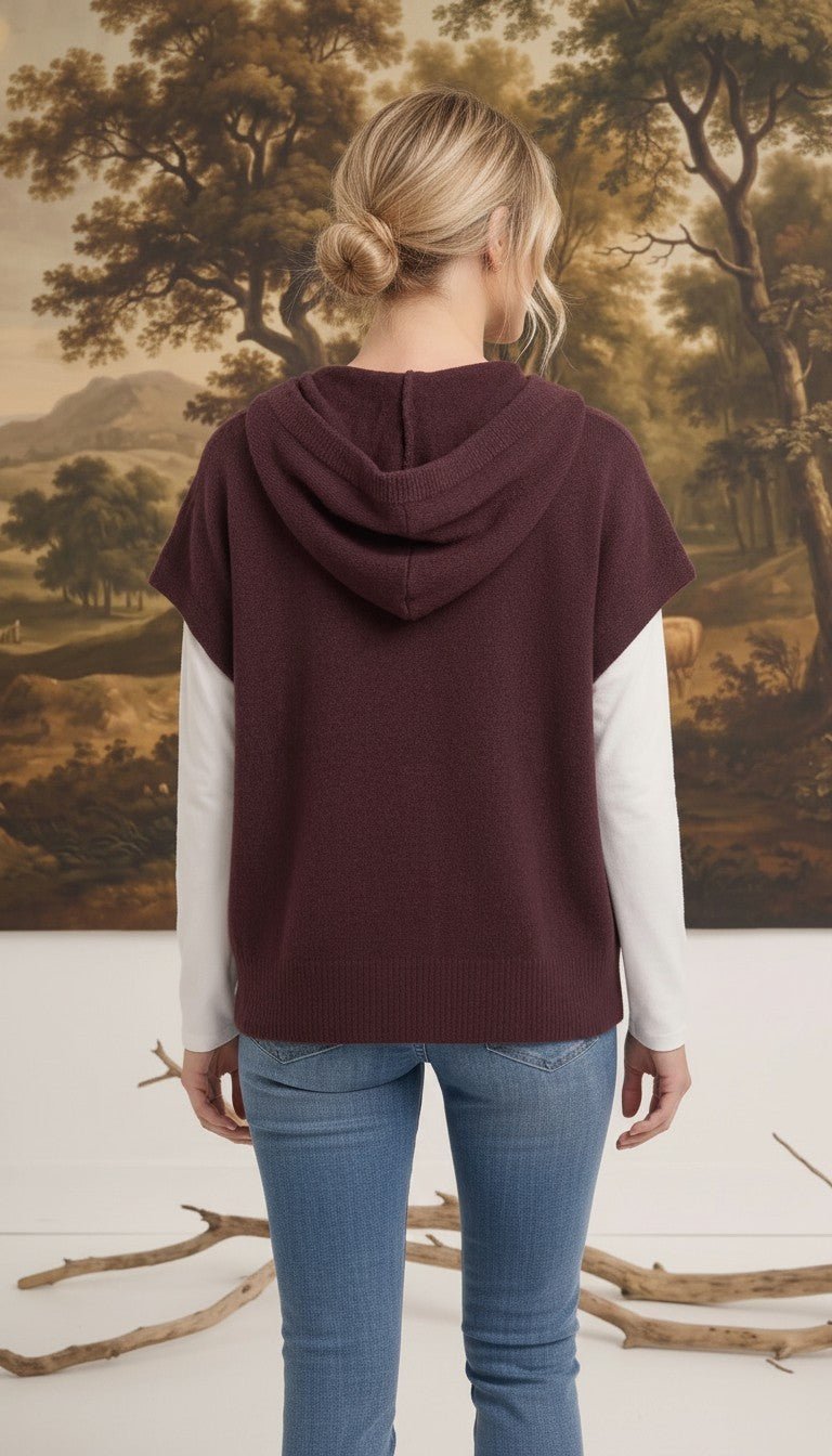 Back view of a woman wearing a graced burgundy button down hoodie top over a white long sleeve shirt and blue jeans