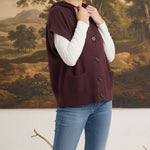 graced burgundy button down sleeveless hoodie with front pockets worn by a woman over a white long sleeve top