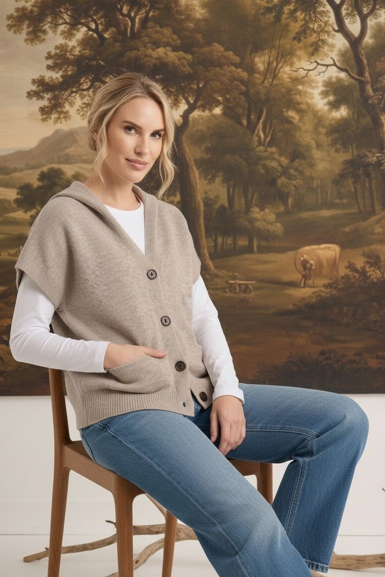 graced taupe button down hooded vest worn over a white long sleeve shirt and blue jeans by a woman on a wooden chair