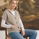 graced taupe button down hooded vest worn over a white long sleeve shirt and blue jeans by a woman on a wooden chair