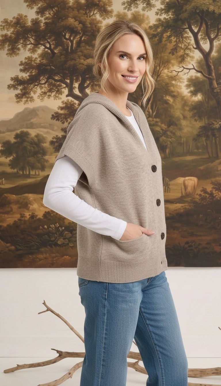 Woman wearing a graced taupe button-down hooded vest over a white long-sleeve shirt and blue jeans