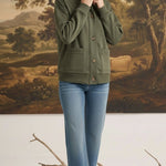 Model wearing a graced olive mock neck button-down cardigan with front pockets and blue jeans in a studio setting