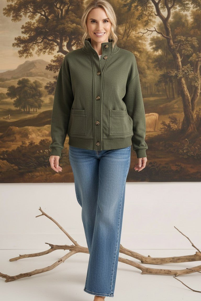 A woman wearing a graced olive green mock neck button-down cardigan with front pockets, paired with blue jeans.