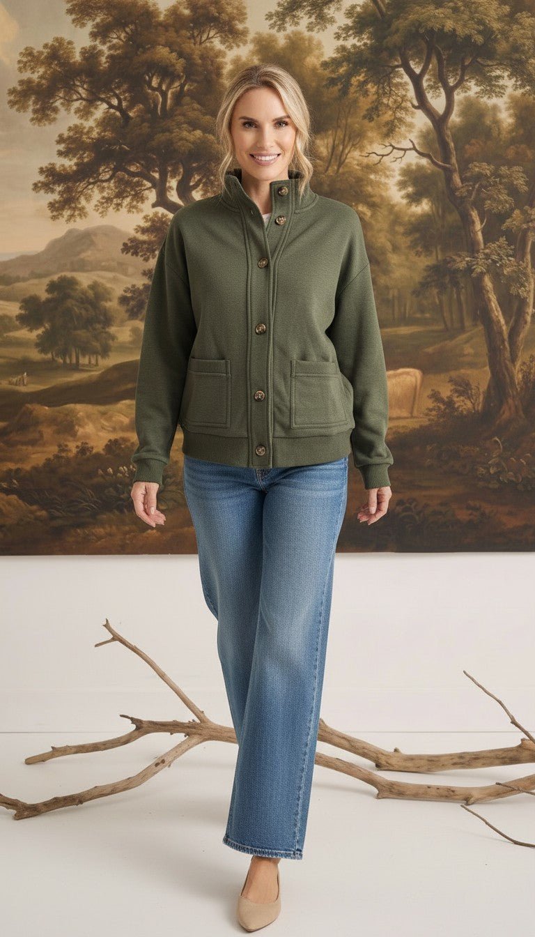 A woman wearing a graced olive green mock neck button-down cardigan with front pockets, paired with blue jeans.
