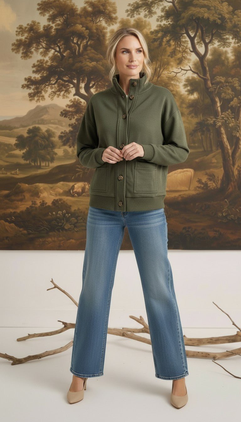 Model wearing a graced olive mock neck button-down cardigan with front pockets, styled with blue jeans and heels.
