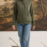 A woman wearing a graced olive green mock neck button-down cardigan with front pockets, paired with blue jeans.