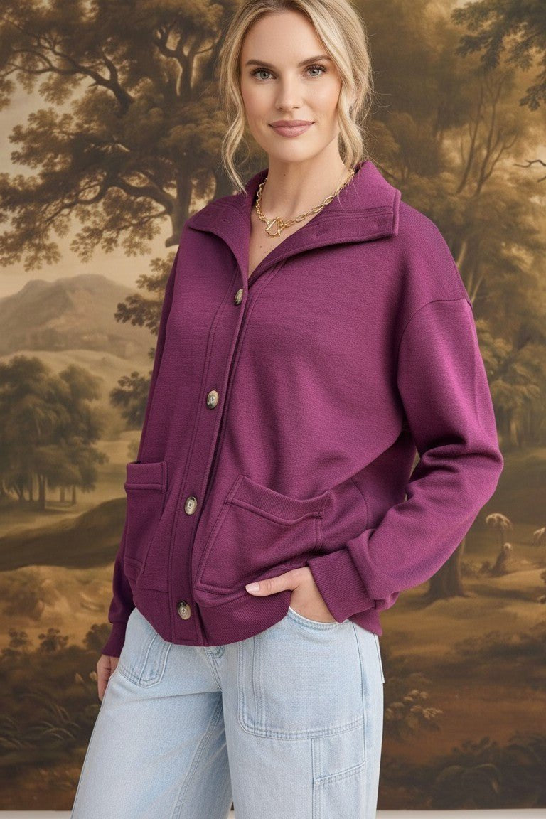 A model wearing a wine-colored graced button-down mock neck cardigan with front pockets and light wash jeans.