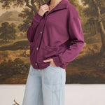 Model wearing a wine-coloured graced button-down mock neck cardigan with front pockets and light wash jeans