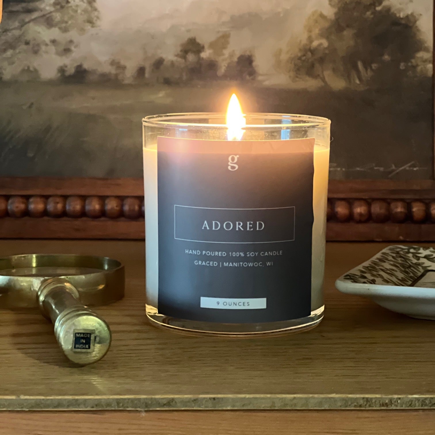 Small graced Adored home fragrance candle in a glass jar with a lit wick, designed for cozy ambiance and stylish decor.