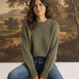A woman wearing a graced chunky olive green crewneck sweater with a textured knit, paired with blue jeans.