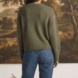 A woman wearing a graced chunky olive green crewneck sweater with a textured knit, paired with blue denim jeans.