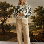 A woman wearing a graced chunky knit navy and cream striped cardigan with buttons, paired with tan trousers.