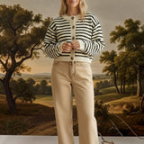 A woman wearing a graced chunky knit navy and cream striped cardigan with buttons, paired with tan trousers.