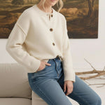 Model wearing a graced cream crew neck cardigan with brown buttons, styled with blue jeans in a cozy indoor setting.