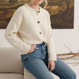 Model wearing a graced cream crew neck cardigan with brown buttons, styled with blue jeans in a cozy indoor setting.