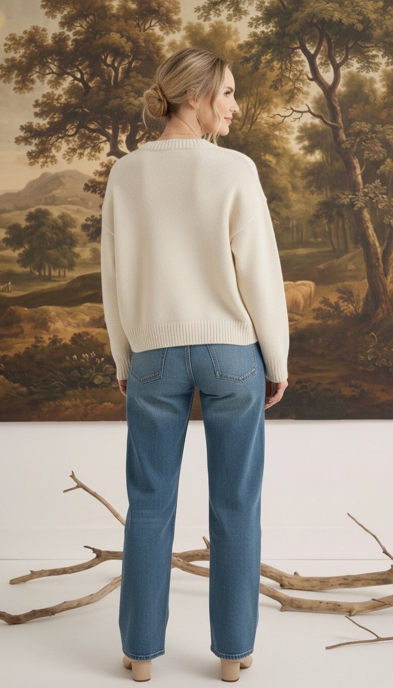 graced cream crew neck cardigan worn by a woman with blonde hair in a bun, paired with blue jeans, back view