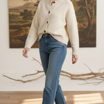 Model wearing a graced cream crew neck cardigan with buttons, paired with blue jeans and beige heels in a studio.