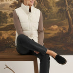 Woman wearing a cream corduroy puffer vest by graced over a brown long-sleeve top and dark jeans in a studio setting.