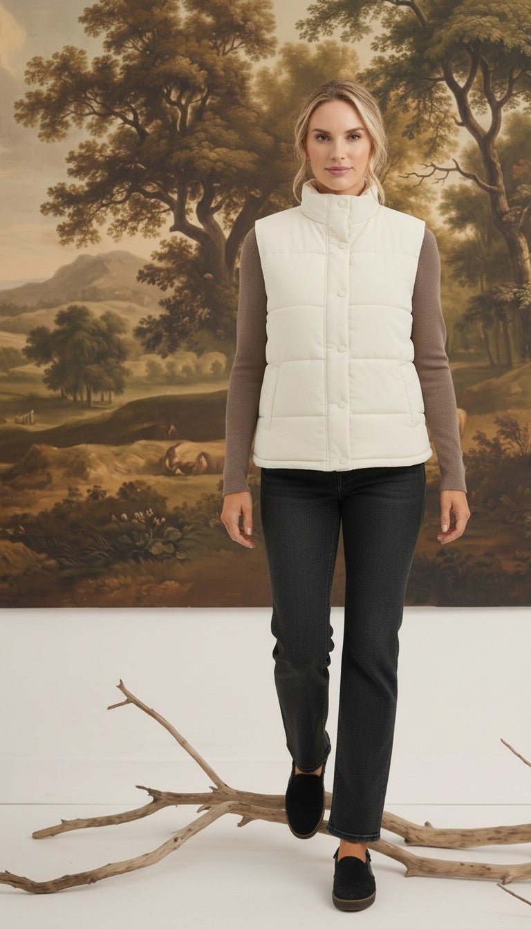 A woman wearing a cream-colored graced corduroy puffer vest over a brown long-sleeve top and dark jeans.