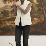 Woman wearing a cream corduroy puffer vest by graced over a brown long-sleeve top and black jeans