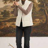 Woman wearing a cream corduroy puffer vest by graced over a brown long-sleeve top and black jeans