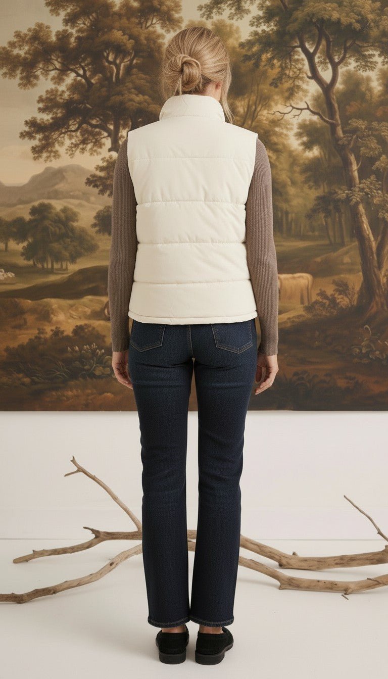 A woman wearing a cream-colored corduroy puffer vest by graced, layered over a brown long-sleeve top and blue jeans.