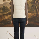 A woman wearing a cream-colored corduroy puffer vest by graced, layered over a brown long-sleeve top and blue jeans.