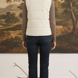 A woman wearing a cream-colored corduroy puffer vest by graced, layered over a brown long-sleeve top and blue jeans.
