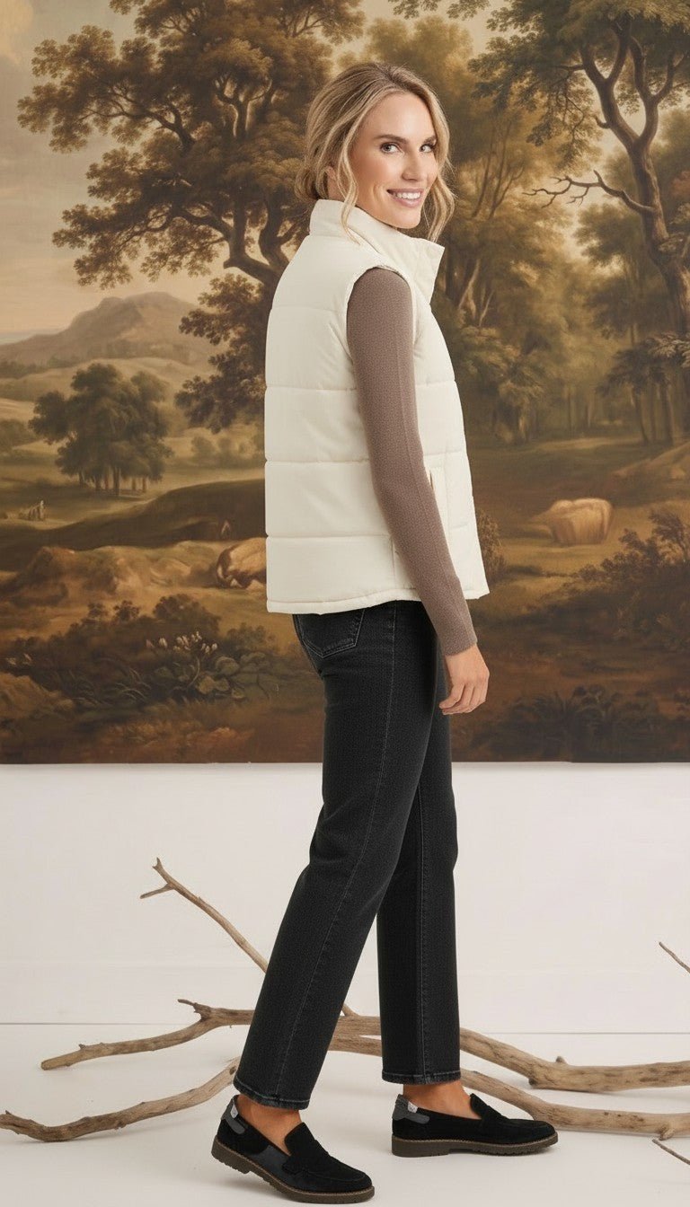 A woman wearing a cream-colored graced corduroy puffer vest over a brown long-sleeve top and black jeans