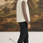 A woman wearing a cream-colored graced corduroy puffer vest over a brown long-sleeve top and black jeans