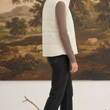 A woman wearing a cream-colored graced corduroy puffer vest over a brown long-sleeve top and black jeans