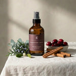 Brown bottle with label on a white tablecloth with cranberries and cinnamon sticks.