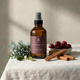 Brown bottle with label on a white tablecloth with cranberries and cinnamon sticks.