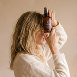 Person wearing a white sweater holding a bottle against a beige background