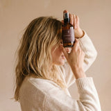 Person wearing a white sweater holding a bottle against a beige background