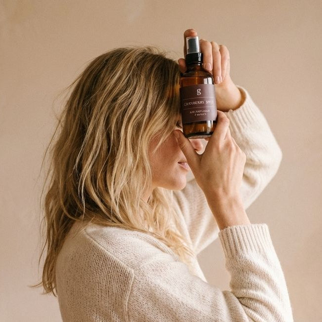 Person wearing a white sweater holding a bottle against a beige background