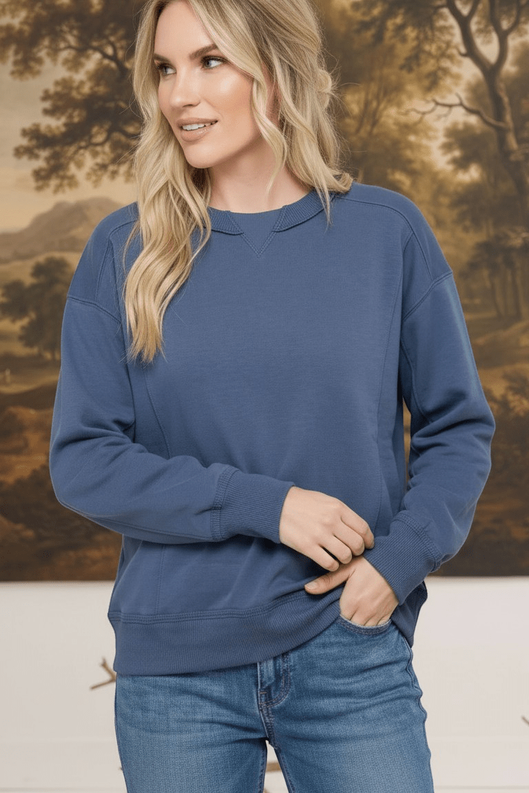 A woman wearing a graced indigo crewneck pullover top with ribbed cuffs and a classic neckline, styled with jeans.